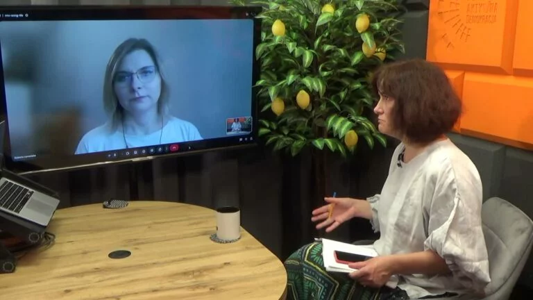 Kadr z nagrania: dwie kobiety rozmawiają zdalnie – jedna widoczna na ekranie laptopa, druga siedzi przy stoliku z notatkami w studiu z drzewkiem cytrynowym