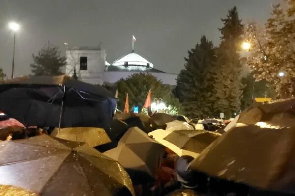 Tłum pod parasolami przed Sejmem wieczorem 22 października