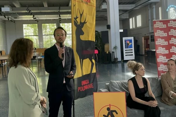 Konferencja o projekcie „UWAGA! Polowanie”, przemawiający z mikrofonem przy banerze z sylwetką jelenia
